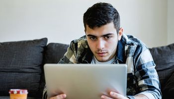 رجل يستخدم الحاسوب المحمول مع رمز درع أمان، يرمز لحماية حسابات الألعاب من الهجمات السيبرانية.