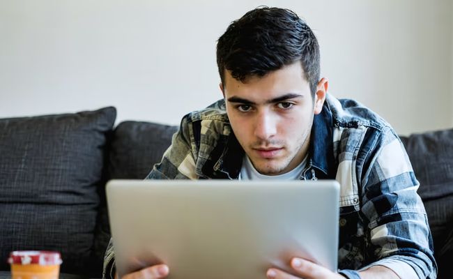 رجل يستخدم الحاسوب المحمول مع رمز درع أمان، يرمز لحماية حسابات الألعاب من الهجمات السيبرانية.